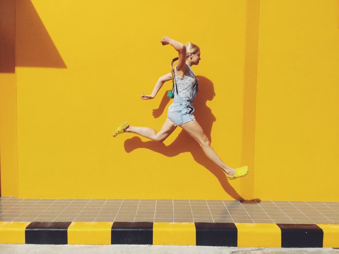 woman jumping on sidewalk with yellow background